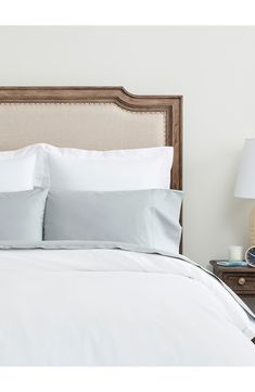 a bed with white sheets and pillows on top of it next to a night stand