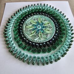 an intricate paper quilling design is displayed on top of a piece of white paper