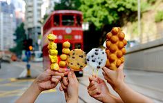 several people holding up food items in front of a red double decker bus on a city street