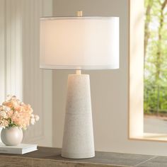 a white table lamp sitting on top of a wooden table next to a vase with flowers