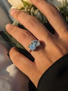 a woman's hand with a ring on her finger and flowers in the background