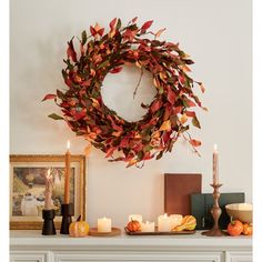 a wreath is hanging on the wall above a mantle with candles and other items in front of it