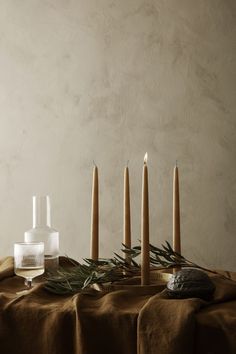 candles and rocks are arranged on a table with a cloth draped over it, along with an arrangement of greenery