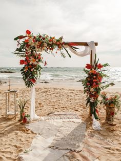 an outdoor wedding set up on the beach with flowers and greenery in front of it