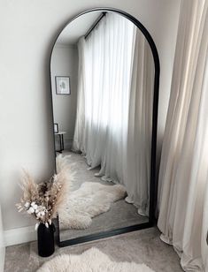 a large mirror sitting on top of a floor next to a vase filled with flowers