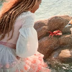 a woman in a white dress standing next to a seagull near the water