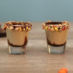 two shot glasses filled with chocolate pudding and sprinkles on top of a wooden table