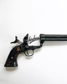 an old revolver with the word kindness on it's side, sitting against a white background