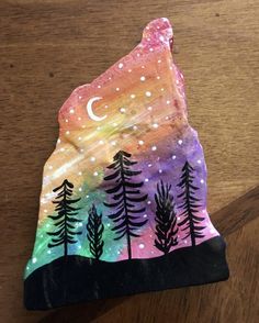 a hand painted rock sitting on top of a wooden table covered in stars and trees