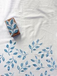 a blue and white table cloth with leaves on it, next to a small wooden block