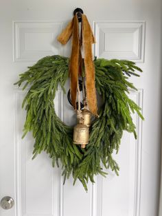 a wreath hanging on the front door with bells attached to it and evergreen leaves around it