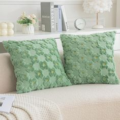 two green pillows sitting on top of a white couch next to a book shelf and lamp