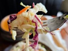 a fork full of food on top of a plate with salad in the middle and another bowl next to it