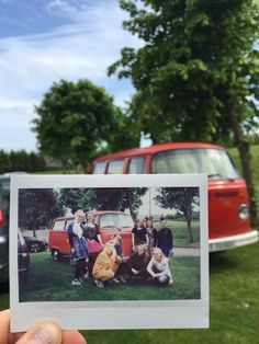 a person holding up a polaroid photo in front of an old vw bus