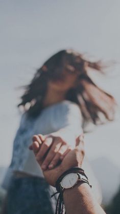 a woman holding onto her wrist with the wind blowing in front of her and she is wearing a watch