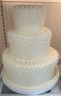 a three tiered white wedding cake with pearls on the top and bottom, sitting on a plate