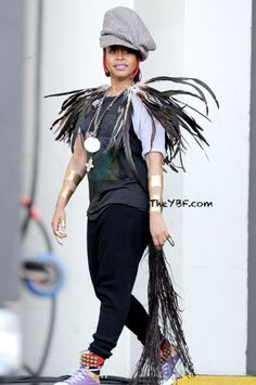 a woman walking down a street while wearing a hat and feathered dress with her hair in the wind