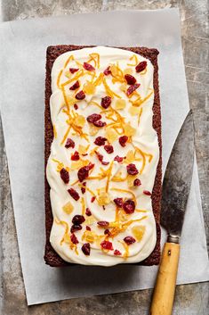 a piece of cake with white frosting and fruit toppings on it next to a knife