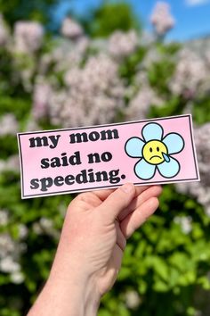 someone holding up a sticker that says, my mom said no speeding in front of some flowers