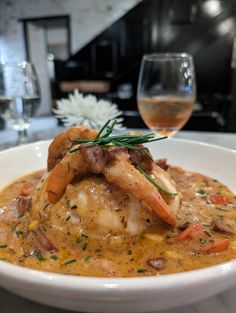 a white bowl filled with food next to a glass of wine