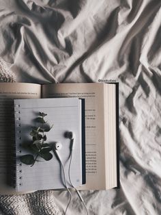 an open book with headphones attached to it on top of a bed covered in sheets