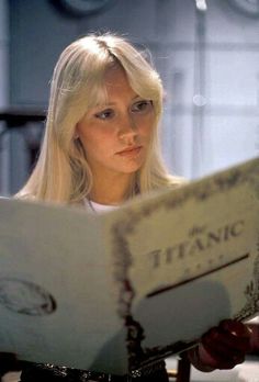 a blonde woman reading a book while sitting at a table