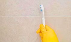 a person in yellow rubber gloves holds a toothbrush against a tiled wall with white tiles