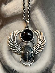 a silver necklace with a scarab beetle on it's back and wings around the neck