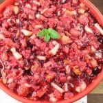 a red bowl filled with lots of food on top of a wooden table next to utensils