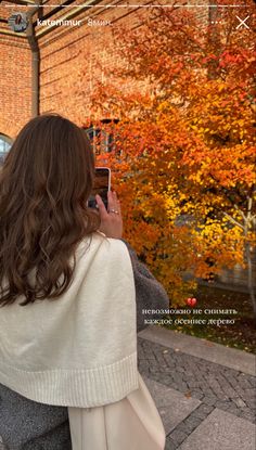 a woman is taking a photo with her cell phone in front of an autumn tree