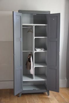 an open gray cabinet with clothes hanging on the door and two shelves in front of it