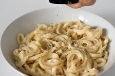 a person is taking a photo of some noodles in a white bowl with a black phone