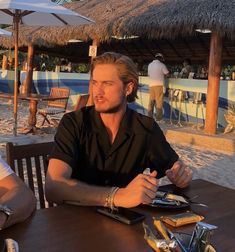 two men sitting at a table with food and drinks in front of them on the beach