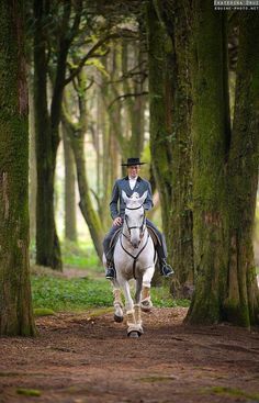 a man riding on the back of a white horse through a forest filled with trees