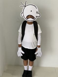 a young boy wearing a white shirt and black shorts standing in front of a wall