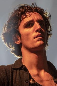 a man with curly hair is staring at something in the distance while wearing a black shirt