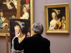 an older woman is painting in front of two paintings