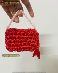 a hand holding a beaded red purse with pearls attached to it's side