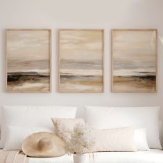 three paintings hang on the wall above a white couch with pillows and a vase filled with flowers