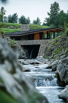 a stream running through a lush green hillside next to a stone covered building with a waterfall coming out of it