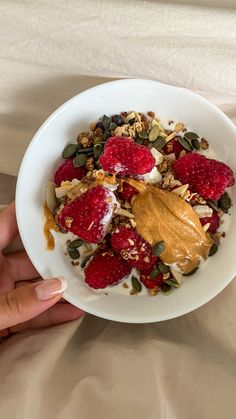 a person is holding a bowl of granola with yogurt and raspberries