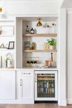 a kitchen with white cabinets and shelves filled with bottles, wine glasses and other items