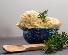 a bowl filled with mashed potatoes next to a wooden spoon and sprig of rosemary