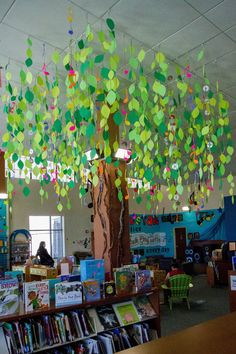 a library filled with lots of books under a tree covered in colorful paper leaves and hanging from the ceiling