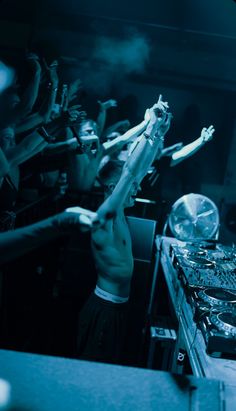 a dj mixing in front of a crowd of people at a club or party with his hands up