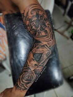 a man's arm with a clock and roses tattoo on it, sitting in a chair