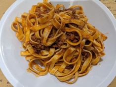 a white plate topped with pasta covered in meat and sauce on top of a wooden table