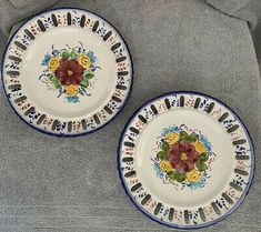 two white and blue plates with flowers on them sitting on a gray cloth covered surface