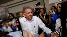 a man in white shirt and black pants shaking hands with people behind him, all holding cameras