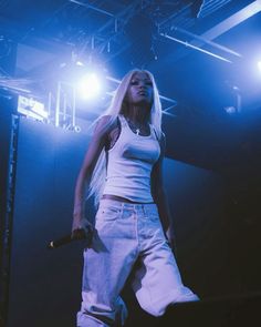 a woman standing on top of a stage with microphones in her hand and lights behind her